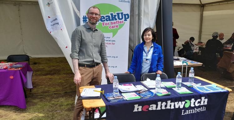 Two people smiling behind a Healthwatch Lambeth desk