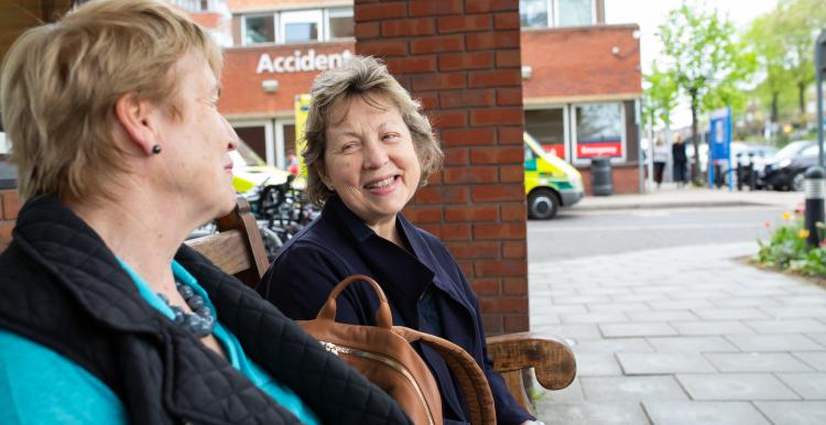 Two women sitting on a bench outside hospital talking