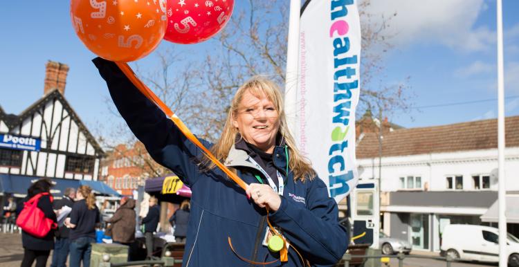 Healthwatch employee holding balloons infront of a Healthwatch sign