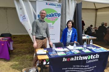 Two people smiling behind a Healthwatch Lambeth desk
