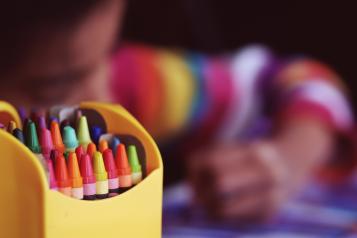 photo of a young child drawing with a box of crayons in foreground