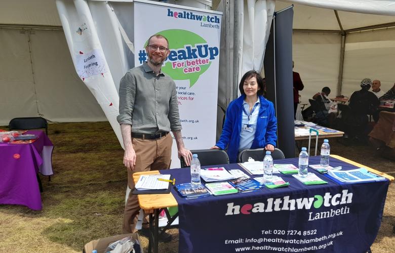Two people smiling behind a Healthwatch Lambeth desk