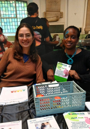 Two people smiling behind a Healthwatch Lambeth desk