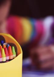 photo of a young child drawing with a box of crayons in foreground